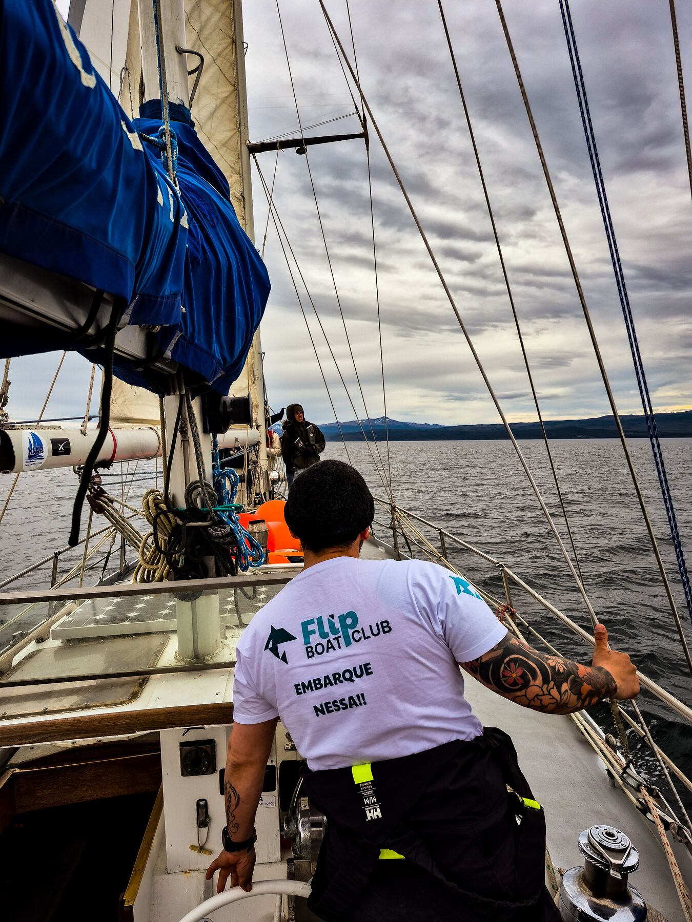 Capitão da expedição ao leme do veleiro, vestindo a camiseta da Flip Boat Club