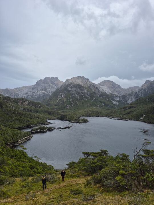 Expedicionários em trilha diante de um lago cercado de montanhas
